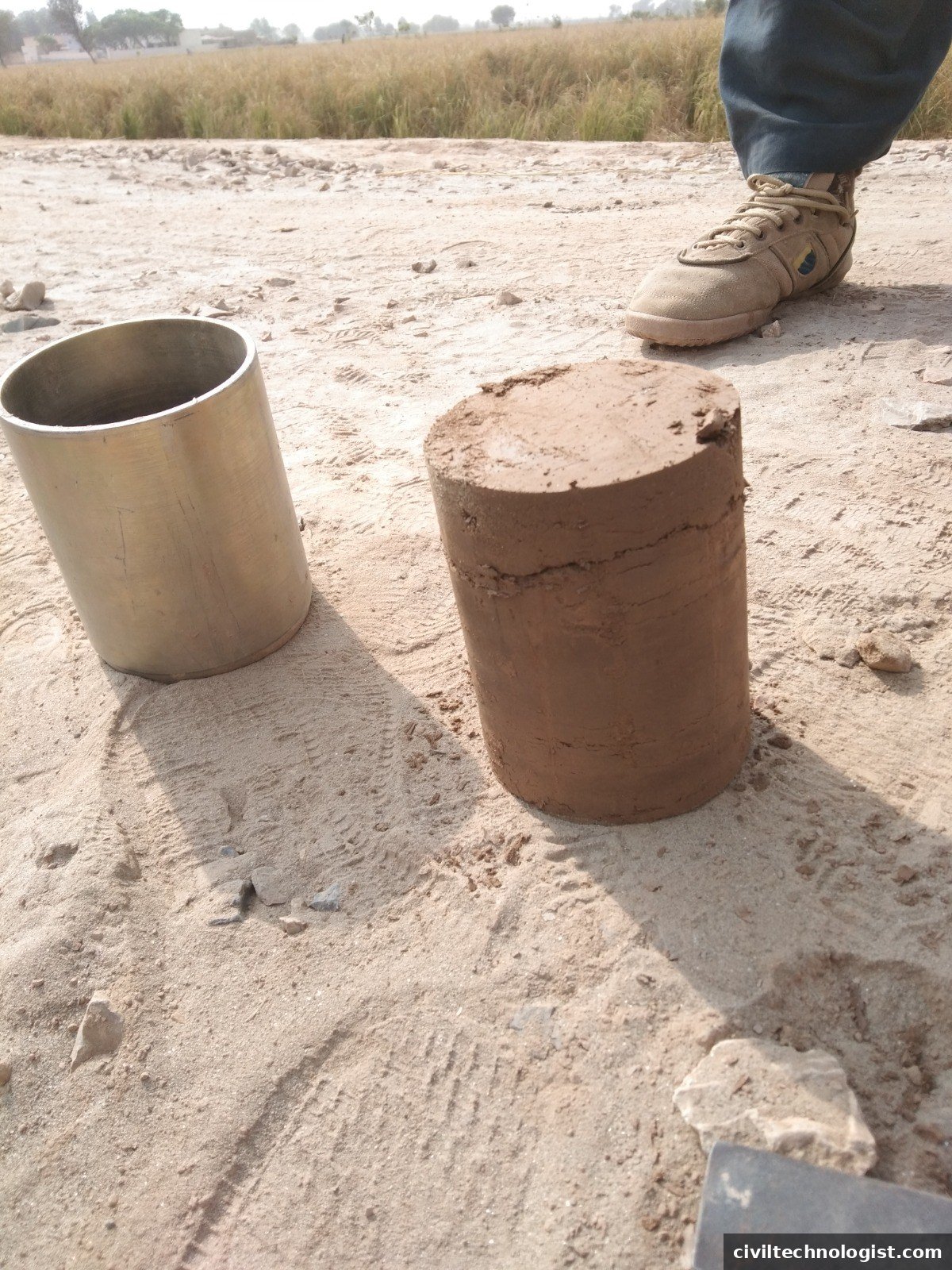 Extracted cylindrical soil core beside an empty core cutter on a construction site in Pakistan